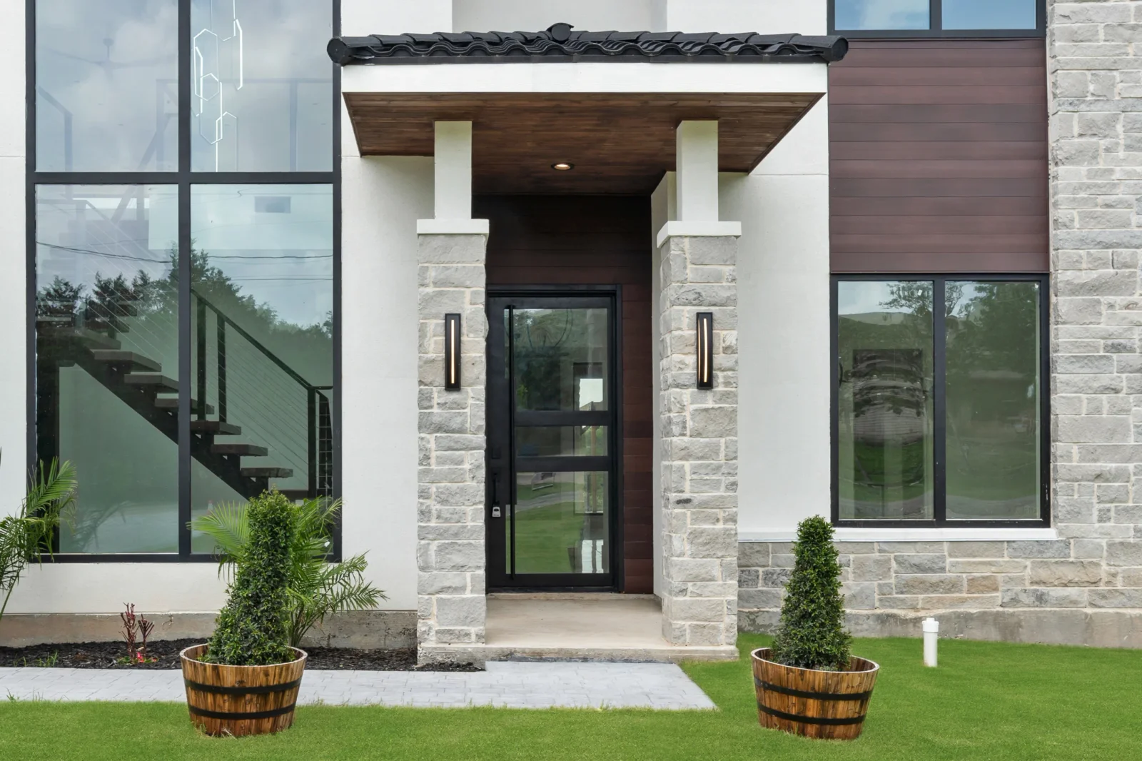 Stone veneer entryway with white columns, dark wood soffit, and black-framed windows