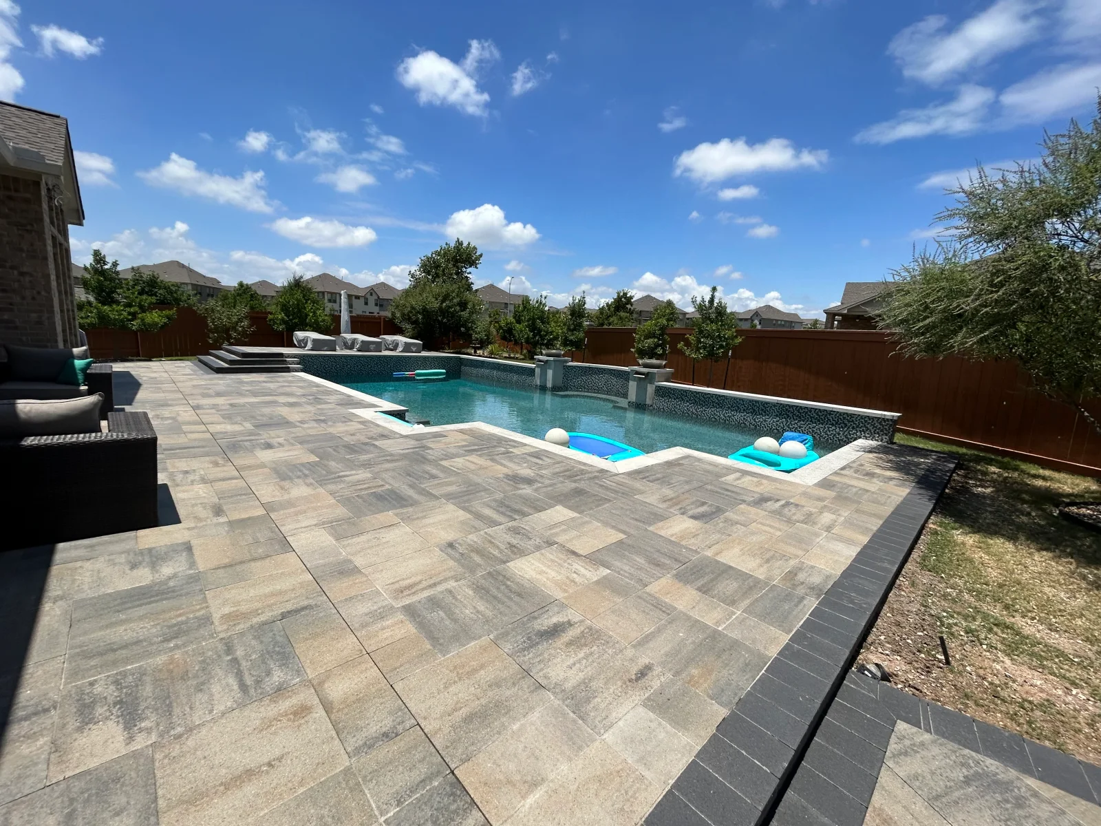 Resort-style pool with dark aggregate finish, spa, and gray porcelain paver patio deck