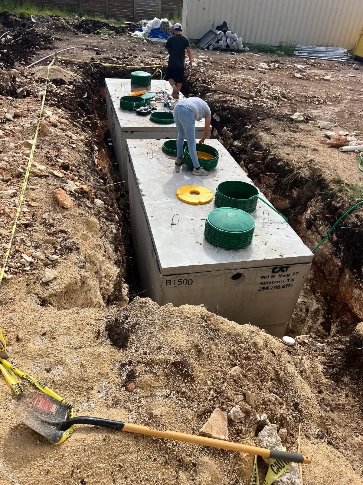 Concrete utility box with green and yellow electrical conduits installed in excavated ground