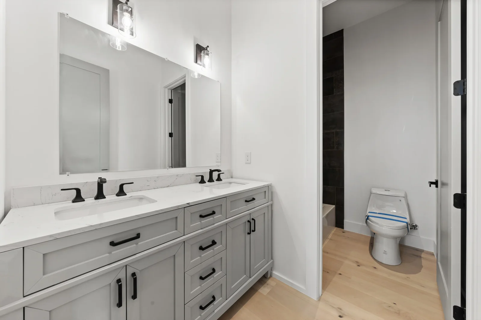 Dual-sink bathroom vanity with gray cabinetry, white quartz counters, and black fixtures