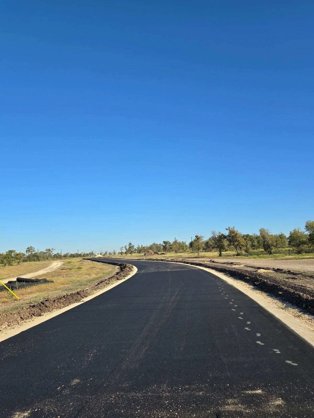 Newly paved asphalt driveway with curved layout and center markings on prepared site