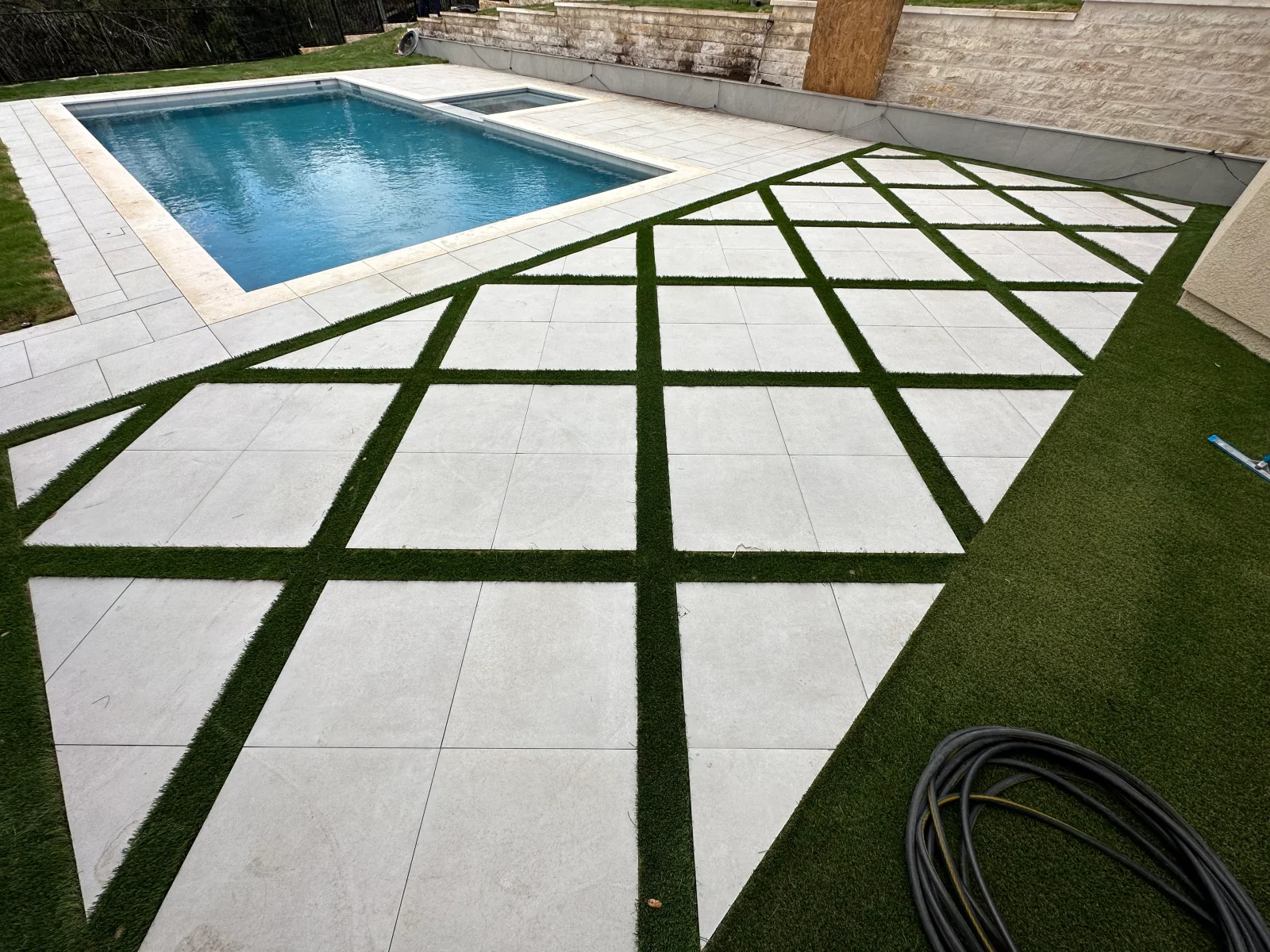 Rectangular pool with light paver deck, geometric turf pattern, and stone retaining wall