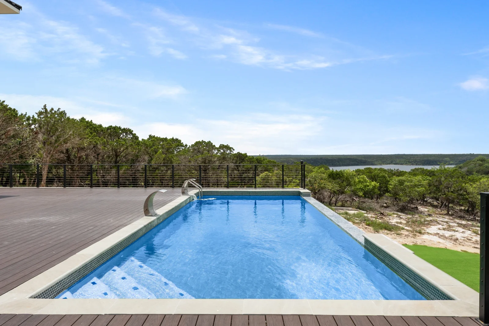 In-ground pool with composite deck, cable railing, and pool cover on hillside overlooking water