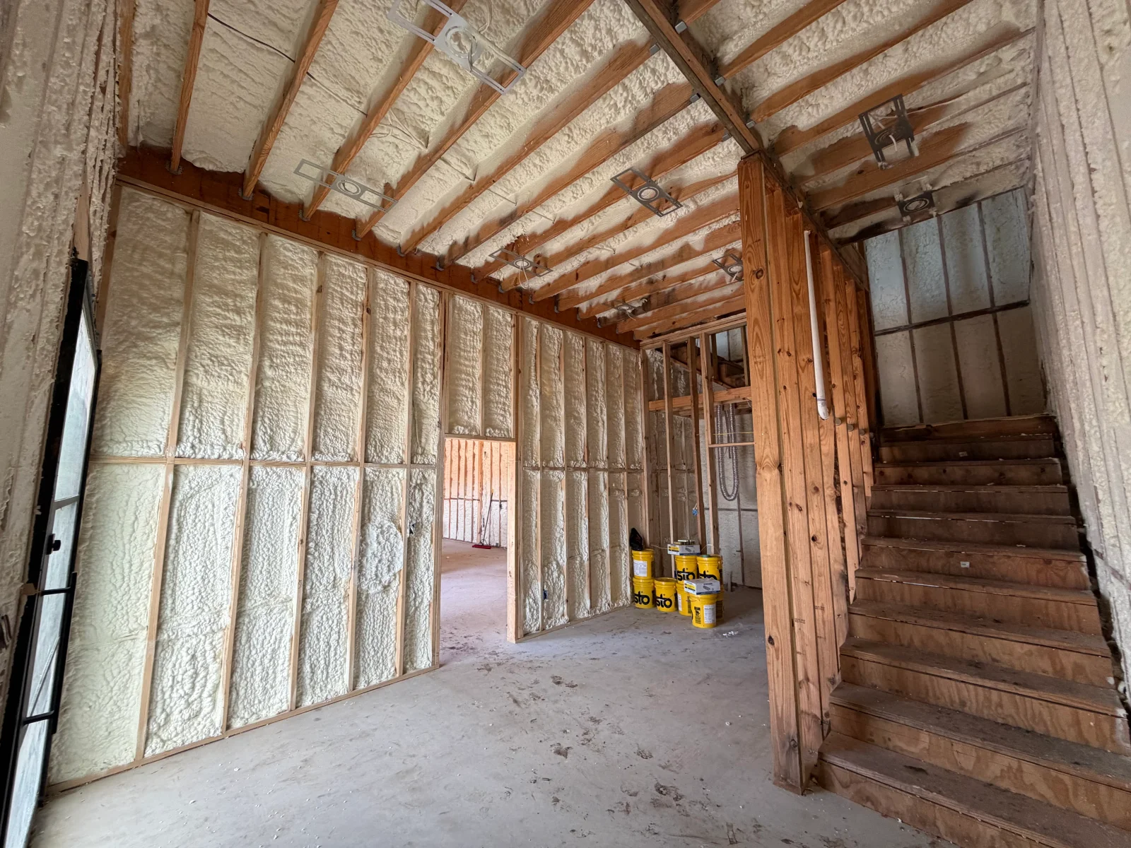Spray foam insulation on walls and ceiling with wooden beam framing and wooden staircase
