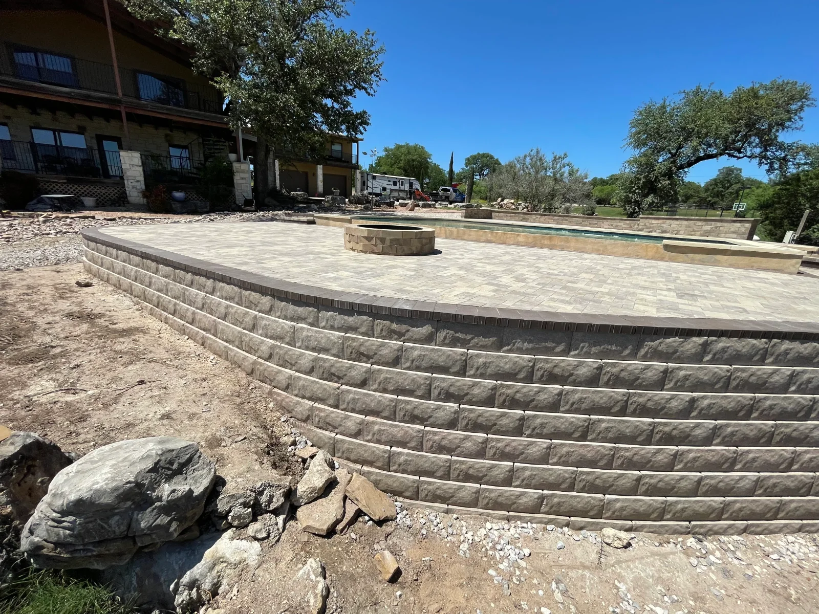 Curved segmental retaining wall and paver patio with fire pit feature under construction