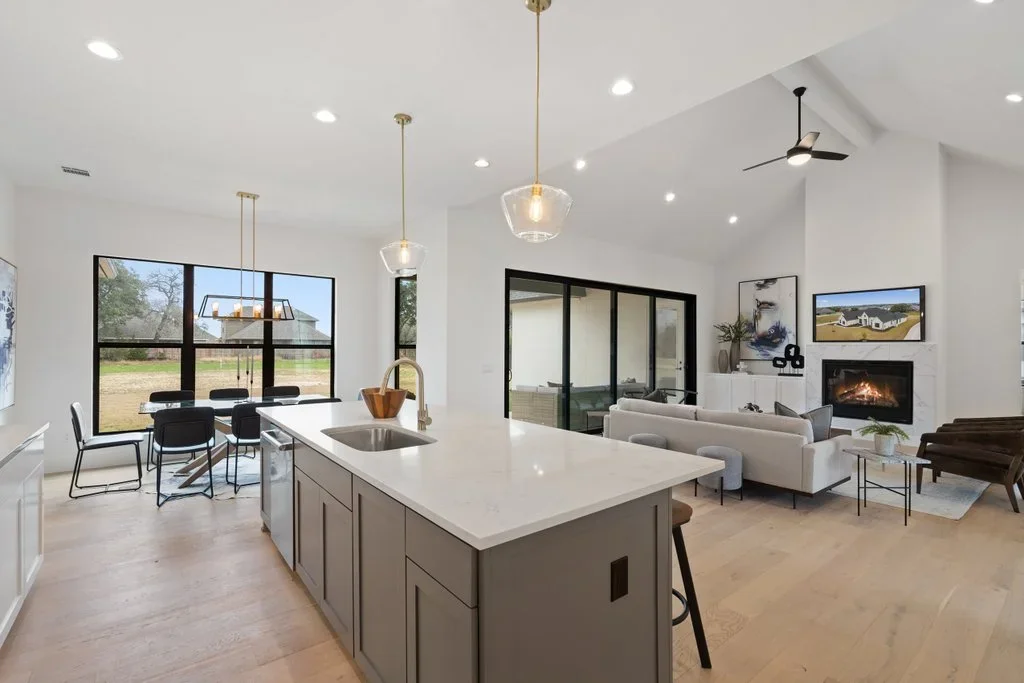 Modern kitchen with white quartz island, custom cabinetry, pendant lights, and open living area with fireplace
