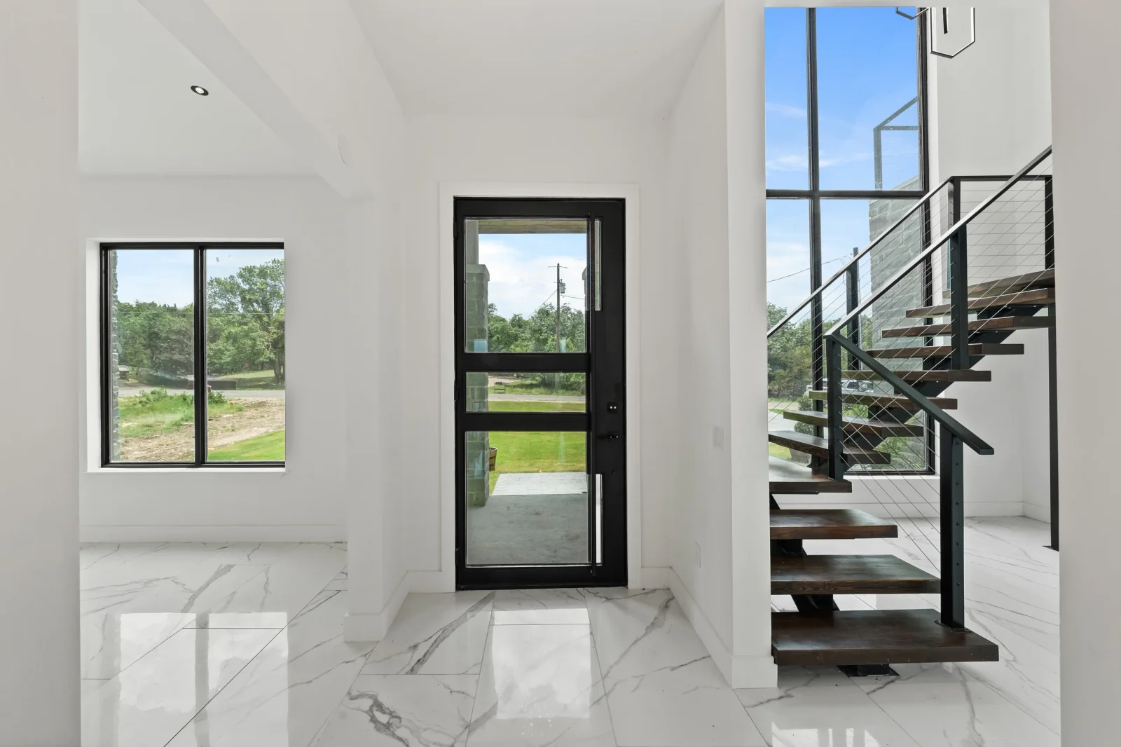 White interior with marble floors, black-framed windows, and modern steel staircase with cable railings