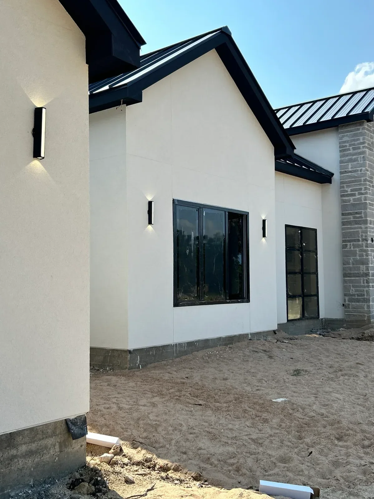 White stucco exterior wall with black metal trim, black-framed windows, and recessed lighting