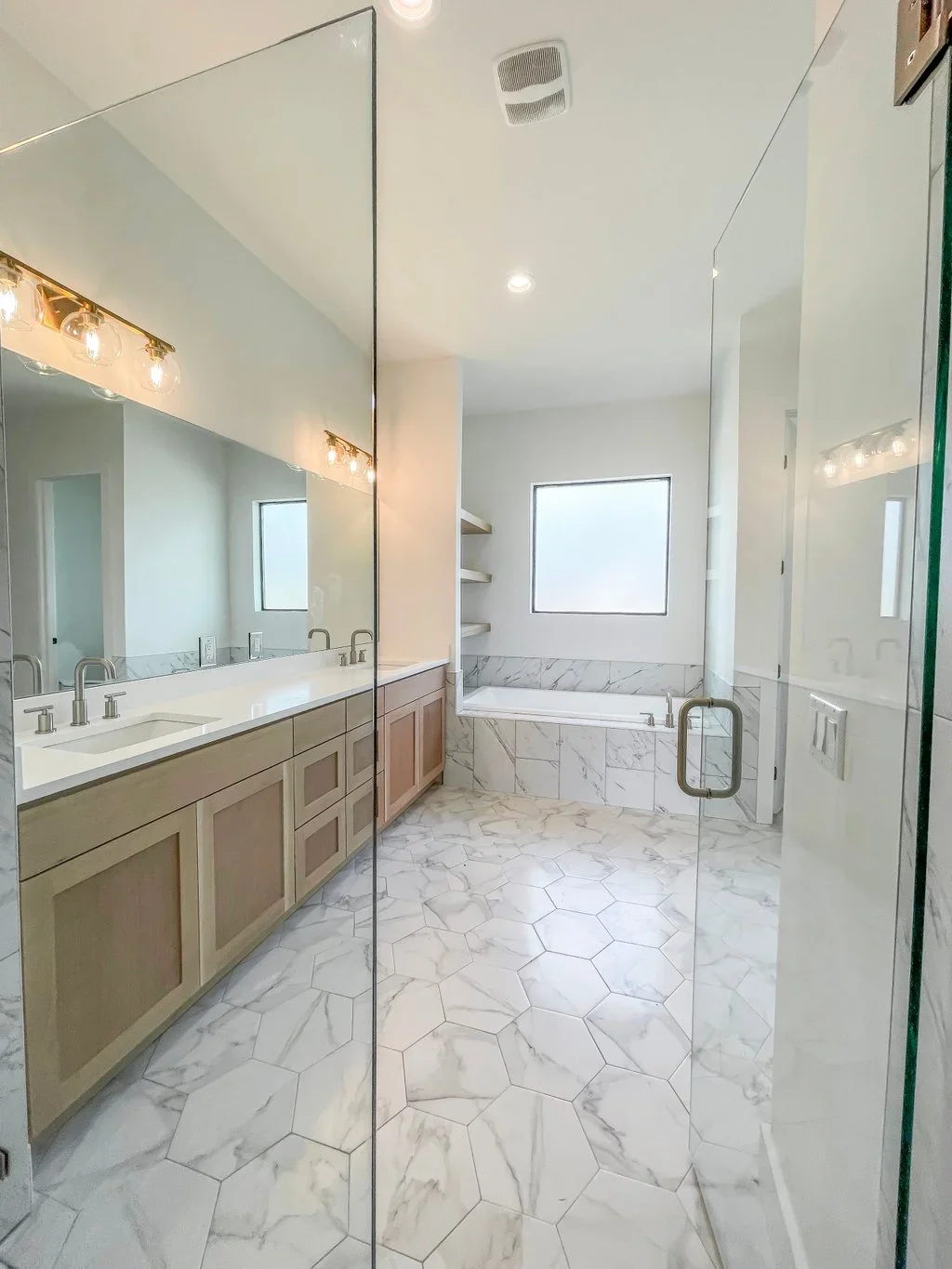 Master bathroom with wood vanity, marble hexagon flooring, and frameless glass shower enclosure